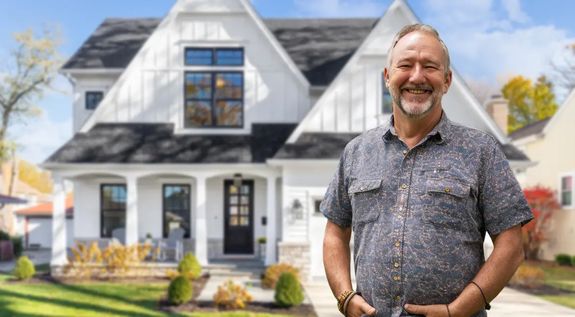 Smiling homeowner standing in front of a modern two-story white house after foundation repair