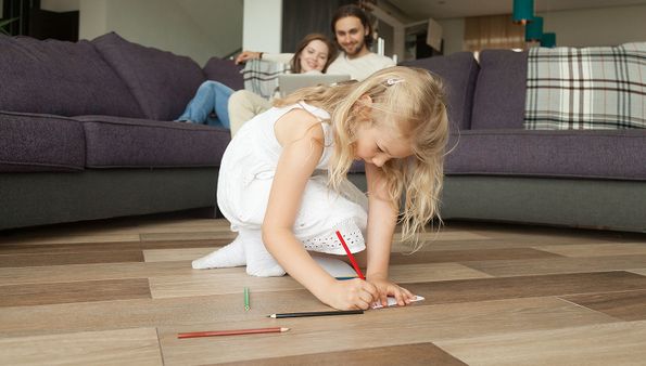 Little girl drawing on new flooring with family in background
