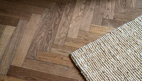 Herringbone-patterned hardwood floor with woven rug edge