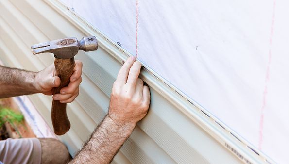 Installing beige vinyl siding with a hammer