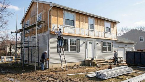 Workers installing new siding on a two-story house