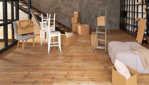 Living space with scratched hardwood flooring and moving boxes
