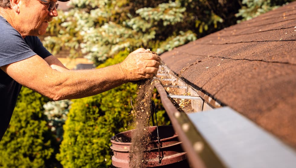 Close-up of a man's hands clearing leaves and debris from a roof gutter.
