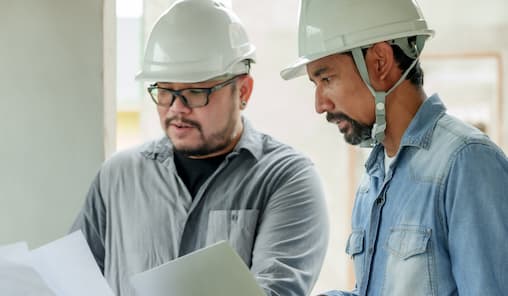 Two men in hard hats examining a blueprint together, focused on their construction project.
