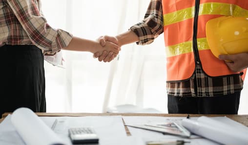 A handshake between two people at a construction site, representing teamwork and agreement in the construction industry.